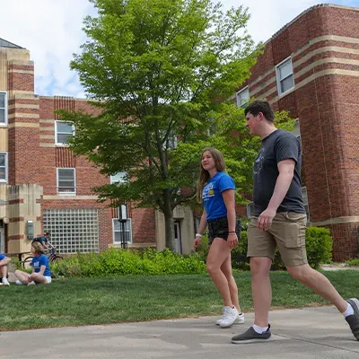 students walk past a dorm building on a sunny day